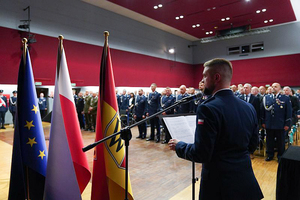 Lektor prowadzący uroczystość zapowiada orkiestrę policyjną. W tle uczestnicy uroczystości.