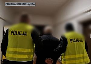 Dwaj policjanci w kamizelkach odblaskowych prowadzą zatrzymanego mężczyznę