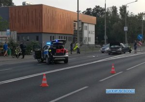 na zdjęciu widać zabezpieczone miejsce wypadku drogowego z udziałem rowerzystki. Widać samochód osobowy a obok policjanta wykonującego oględziny miejsca zdarzenia