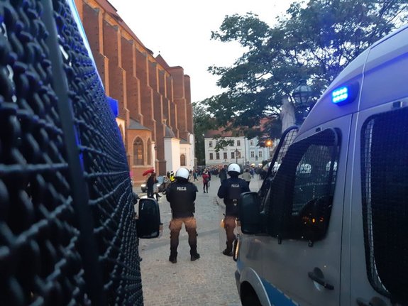 Policjanci w mundurach i kaskach ochronnych pilnują bezpieczeństwa na zgromadzeniu.