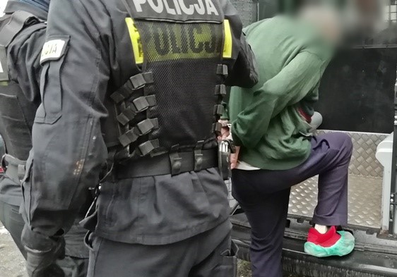 Na zdjęciu dwaj policjanci umieszczają zatrzymanego mężczyznę w radiowozie.