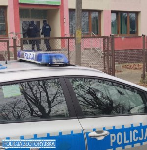 Na zdjęciu na pierwszym planie radiowóz w tle policjanci stojący na klatce przed wejściem do bloku.