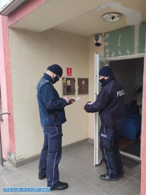 Na zdjęciu dwóch policjantów wchodzi do klatki w bloku.