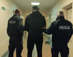Na zdjęciu dwóch policjantów prowadzi zatrzymanego mężczyznę.