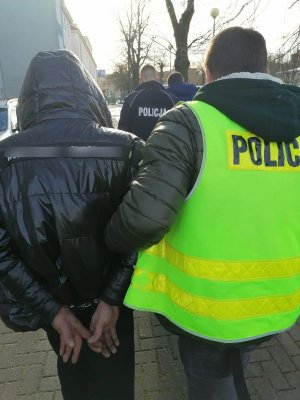 zatrzymany mężczyzna prowadzony w kajdankach przez policjanta