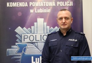 zdjęcie policjanta na tle banera Komendy Powiatowej Policji w Lubiniu