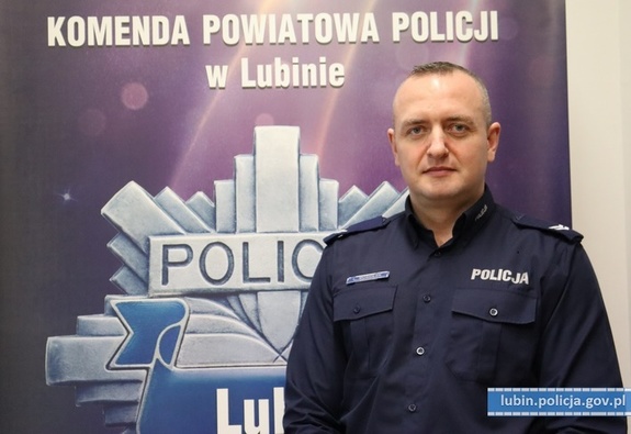 zdjęcie policjanta na tle banera Komendy Powiatowej Policji w Lubiniu