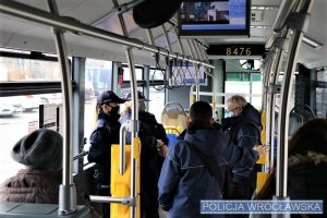 Zdjęcie przedstawia wnętrze autobusu z pasażerami, w środku znajduje się policjantka w mundurze oraz pracownik MPK