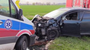 Zdjęcie przedstawia przód karetki pogotowia oraz stojący obok rozbity wrak samochodu biorący udział w wypadku.