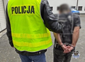 Policjant w kamizelce prowadzi zatrzymanego mężczyzne