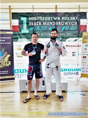 na zdjęciu widać dwóch zawodników z medalami na szyi, w tle widać podium