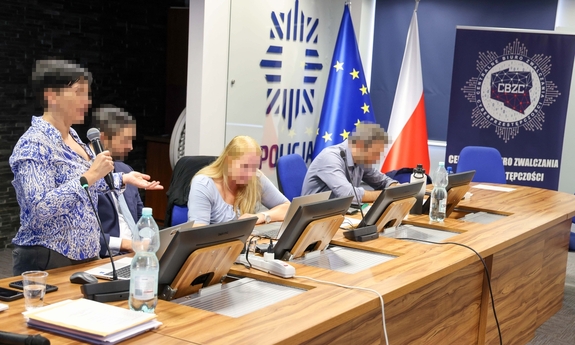 kobieta stoi przy stole prezydialnym przemawiając z mikrofonem w dłoni