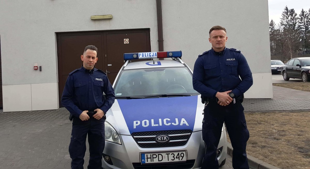 Policjanci stoją przed radiowozem.