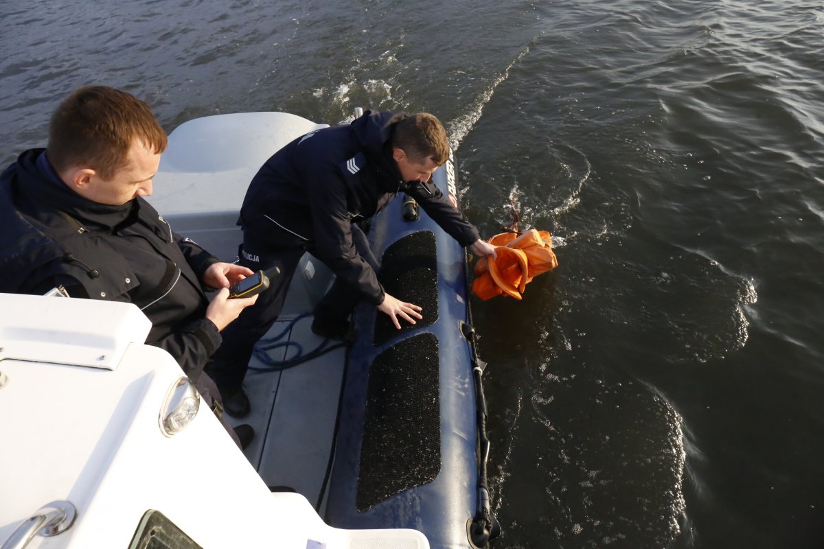 policjant na łodzi wyjmuje kapok z wody, drugi z nich trzyma telefon