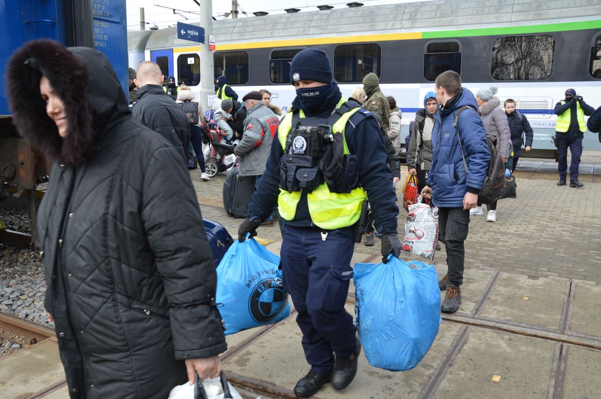 na dworcu policjant pomaga uchodźcom nieść bagaże