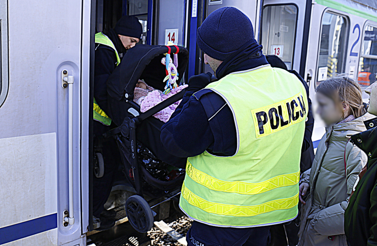 Policjanci pomagają wnieść wózek z dzieckiem do wagonu.