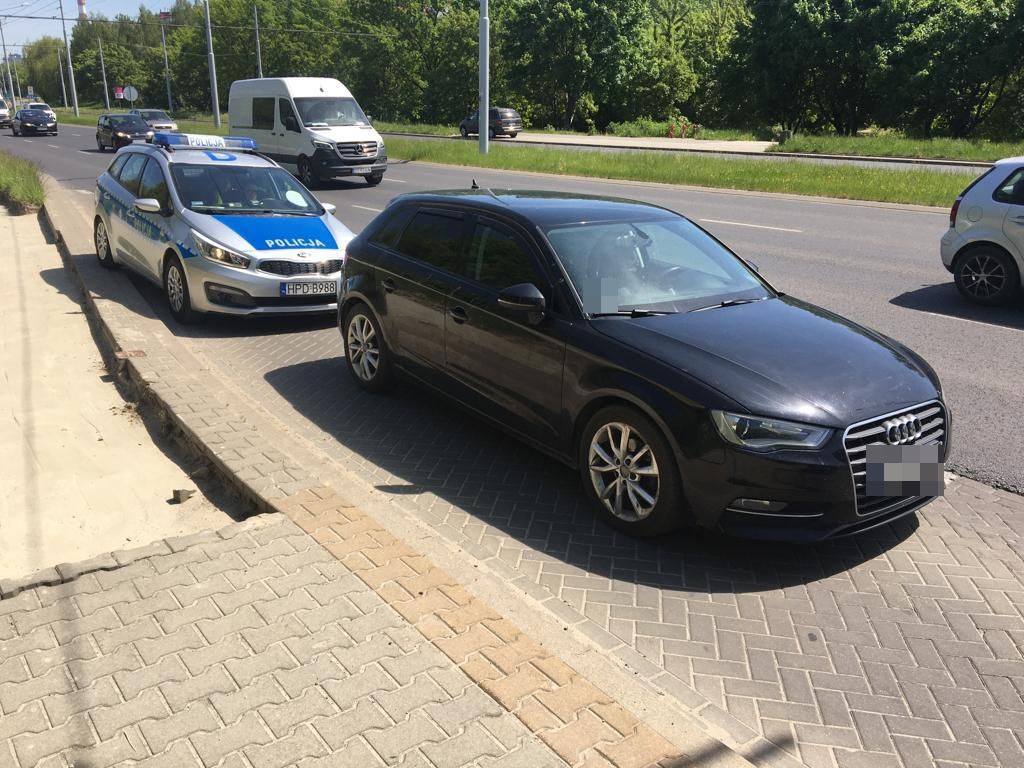 Na zdjęciu stoi czarne audi oraz oznakowany radiowóz.