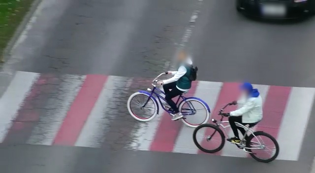 Dwoje rowerzystów przejeżdża przez przejście dla pieszych.