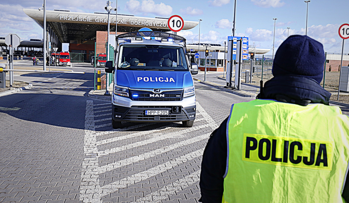 Zdjęcie przedstawia policjanta, radiowóz oznakowany na przejściu granicznym w Dołhobyczowie.