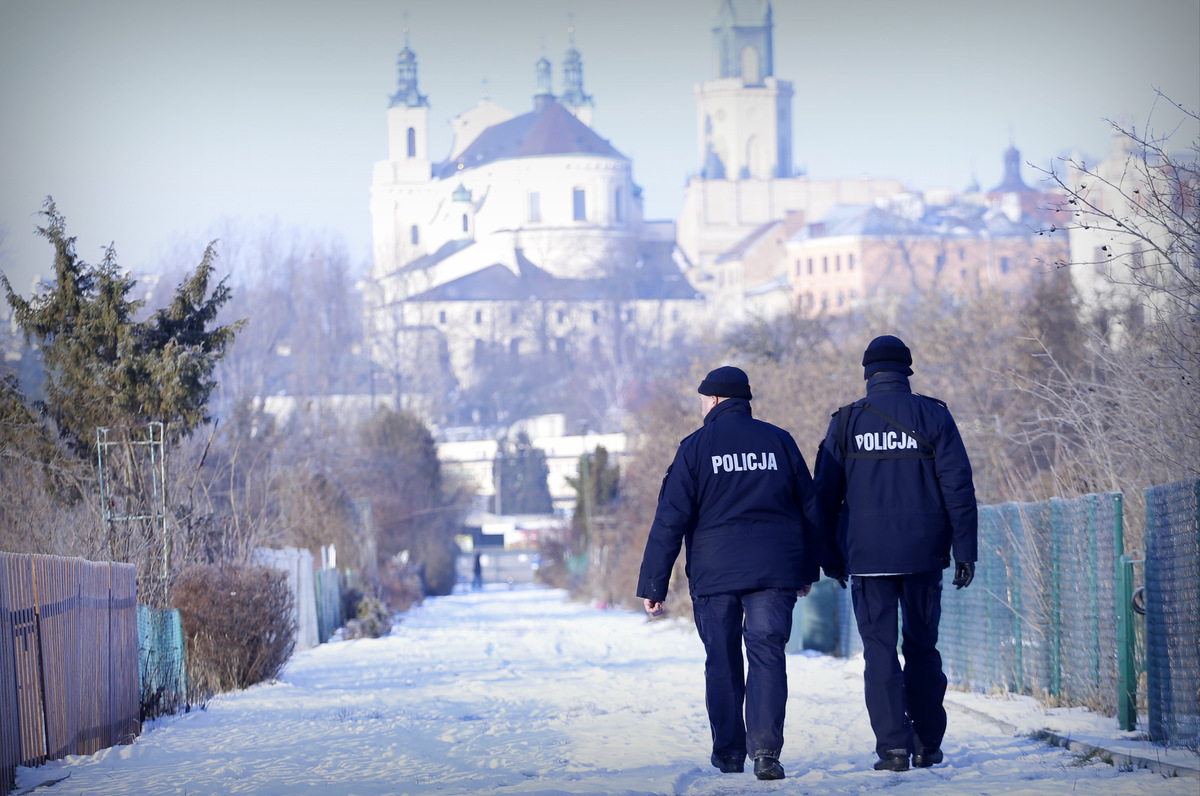 Zdjęcie przedstawia dwóch umundurowanych policjantów patrolujących ogródki działkowe w Lublinie.