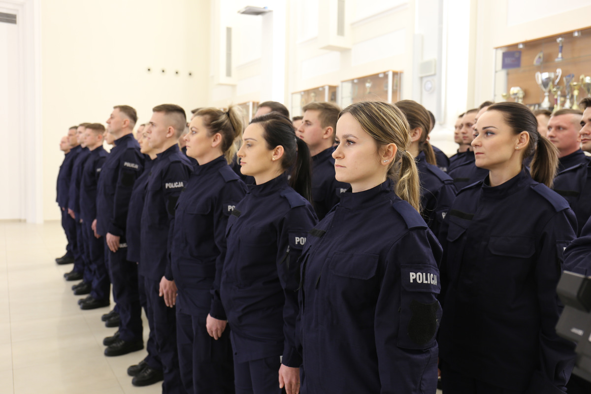 Nowi funkcjonariusze podczas uroczystości ślubowania ubrani w granatowe mundury z napisami policja.