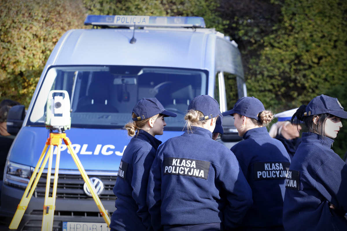 W pierwszym planie zdjęcia widzimy uczennice z kalsy policyjnej. W głębi zdjęcia oznakowany radiowóz.
