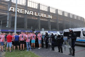 policjanci przed stadionem i kibice przed  wejściem na mecz