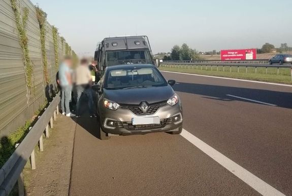 Policjanci kryminalni podczas zatrzymania oszustów na obwodnicy miasta. Samochód marki renault, a z tyłu policyjny bus.