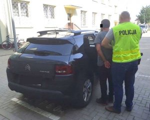 policjant doprowadza mężczyznę podejrzanego o kradzież samochodu