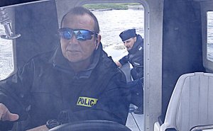 policjant za sterami łodzi, w tle drugi mundurowy