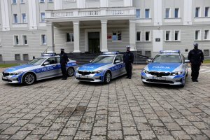 policjanci stojący na baczność przy radiowozach