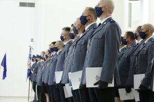 Policjanci ustawieni w szeregu trzymają w ręku akty nominacji na stopień oficerski.