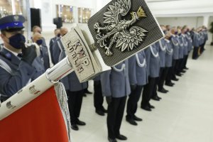 W pierwszym planie zdjęcia grot sztandaru Komendy Wojewódzkiej Policji w Lublinie na nim umieszczony jest wizerunek orła ustalony dla godła Rzeczypospolitej Polskiej z napisem KWP LUBLIN.
W drugim planie zdjęcia stoją funkcjonariusze policji do odznaczenia.