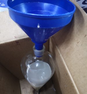 niebieski lejek wpuszczony w szklane naczynie z białym płynem