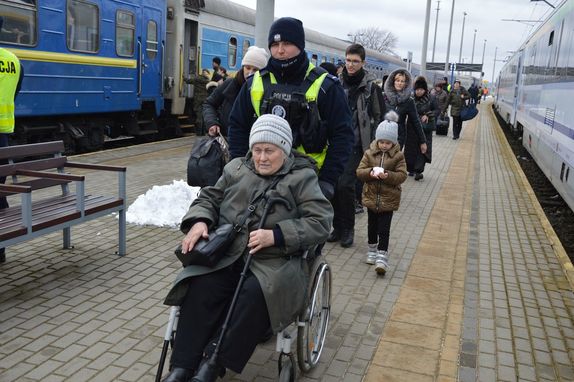na dworcu policjant pcha wózek inwalidzki na którym siedzi starsza kobieta
