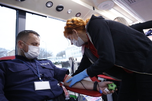 Funkcjonariusz ubrany w mundur z napisami policja oddaje krew w mobilnym punkcie.