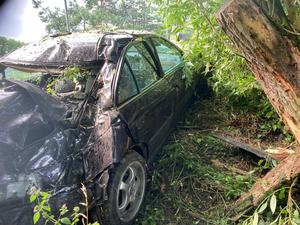 Pojazd Honda po wypadku pod drzewem. W tle policjant