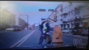 zdjęcie obrazu monitora kamery pojazdu nieoznakowanego policji. Na zdjęciu na pierwszym planie policjant przeprowadzający przez jezdnie starsza kobietę. policjant niesie w ręku siatkę z zakupami kobiety.