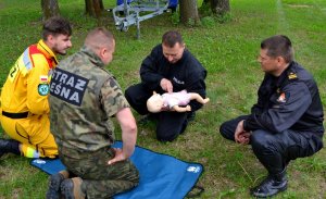 Policjant reanimuje manekina (dziecko), wokół przyglądają się inni uczestnicy szkolenia.