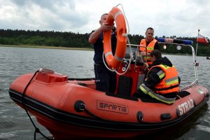 Policjant trzyma koło ratunkowe. Znajduje się na łodzi ratunkowej razem z ratownikami.