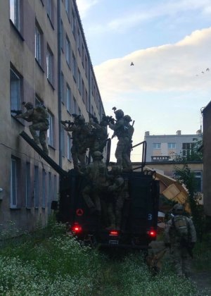 policjanci wchodzący przez okno do budynku przy użyciu specjalnego pojazdu z drabinką