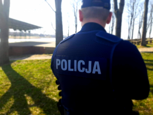 Policjant prewencji stoi tyłem, a w tle wschodzące słońce.