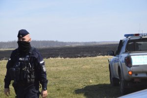 Policjant podczas działań. W tle radiowóz.