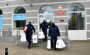 Policjanci noszą prezenty. W tle budynek komendy Policji.