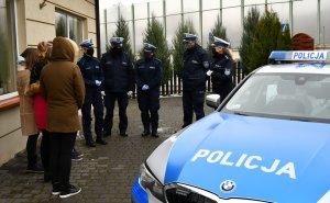 Policjanci przekazują podarunki obdarowanym. W tle widać radiowóz.