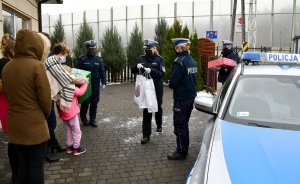 Policjanci przekazują podarunki obdarowanym. W tle widać radiowóz.