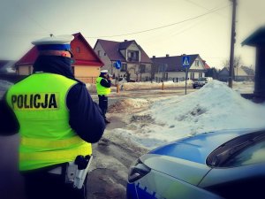 Policjanci stoją przy przejściu dla pieszych na tle radiowozu.