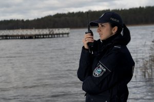 Policjantka rozmawia przez stacje. W tle jezioro.