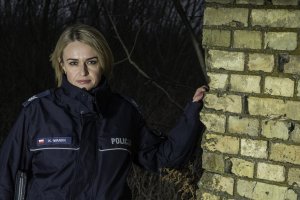 Policjantka pozuje do zdjęcia przy murze ze starej cegły.