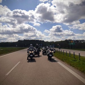 Grupa policyjnych motocyklistów stoi na lewym pasie ruchu.